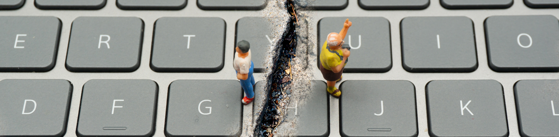 Two human figurines stand on a keyboard facing away from each other on either side of a crack.